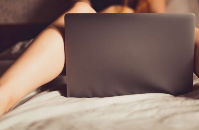 Picioarele unei tinere, pe un pat, cu un laptop intre ele